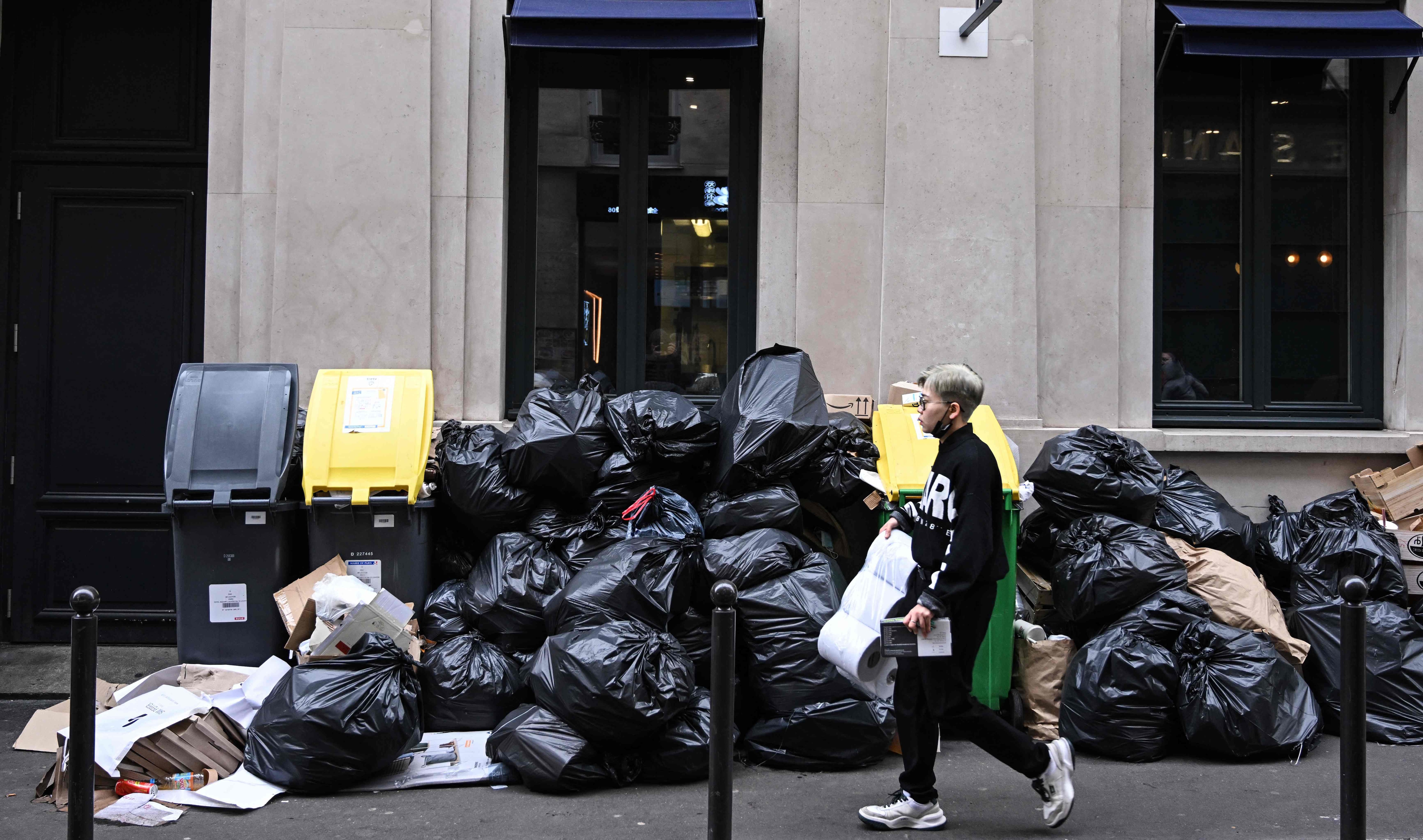 A pedestrian walks past household waste containers in a street of Paris, on March 12, 2023, which have been piling up since collectors went on strike against the French government's proposed pensions reform on March 6, 2023. (Photo by Stefano RELLANDINI / AFP)