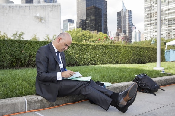 Mann im schwarzen Anzug sitzt in New York auf dem Bürgersteig und macht sich Notizen