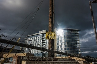 Sunlit building in the background. In the foreground a poster stapled to a post reads: turn to Jesus.