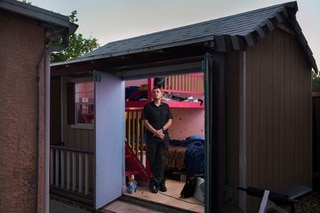 Doors of small building opened with a person standing inside, looking at the camera.