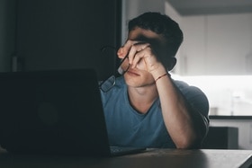 Ein Mann sitzt im Dunkeln vor seinem Computer, seine Körpersprache zeigt Resignation an