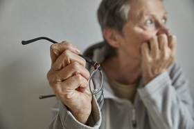 Femme âgée tenant ses lunettes d un air préoccupé