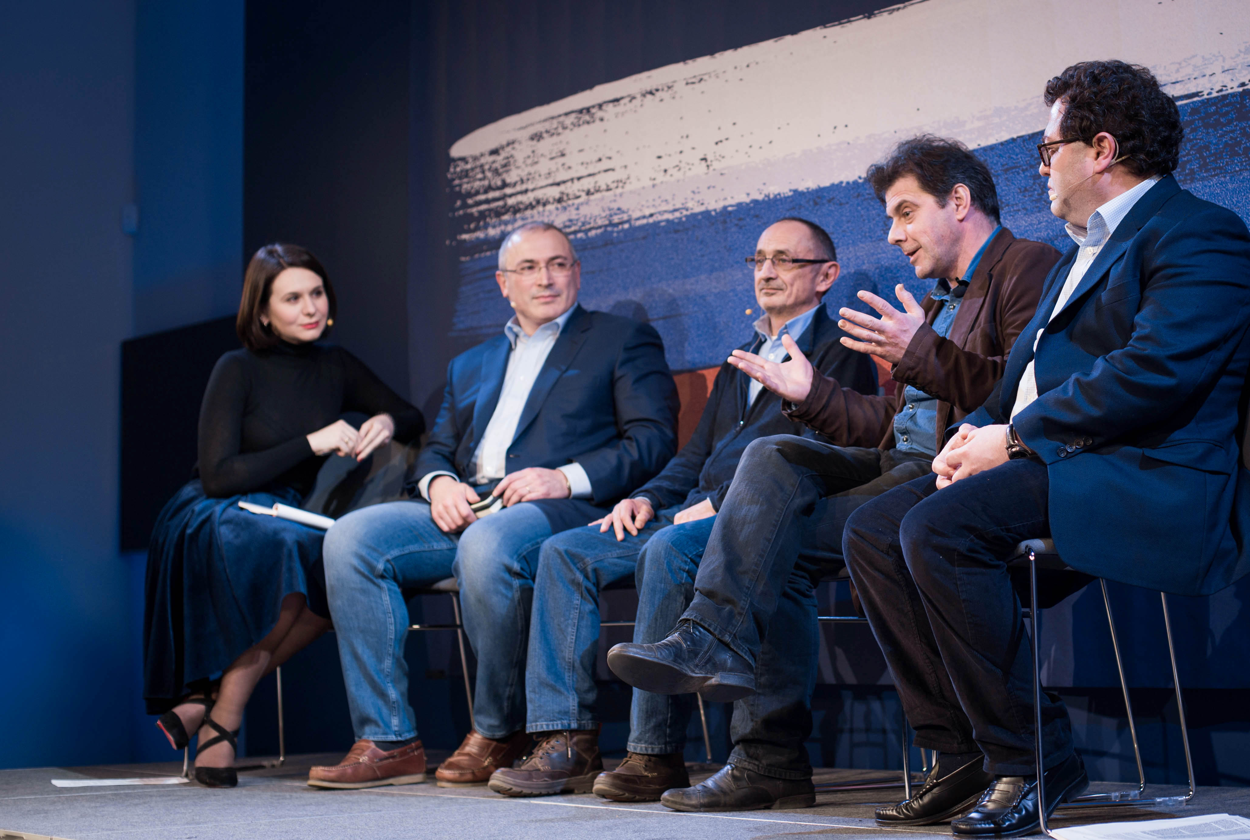 Quatre hommes et une femme assis sur un podium pour un débat.