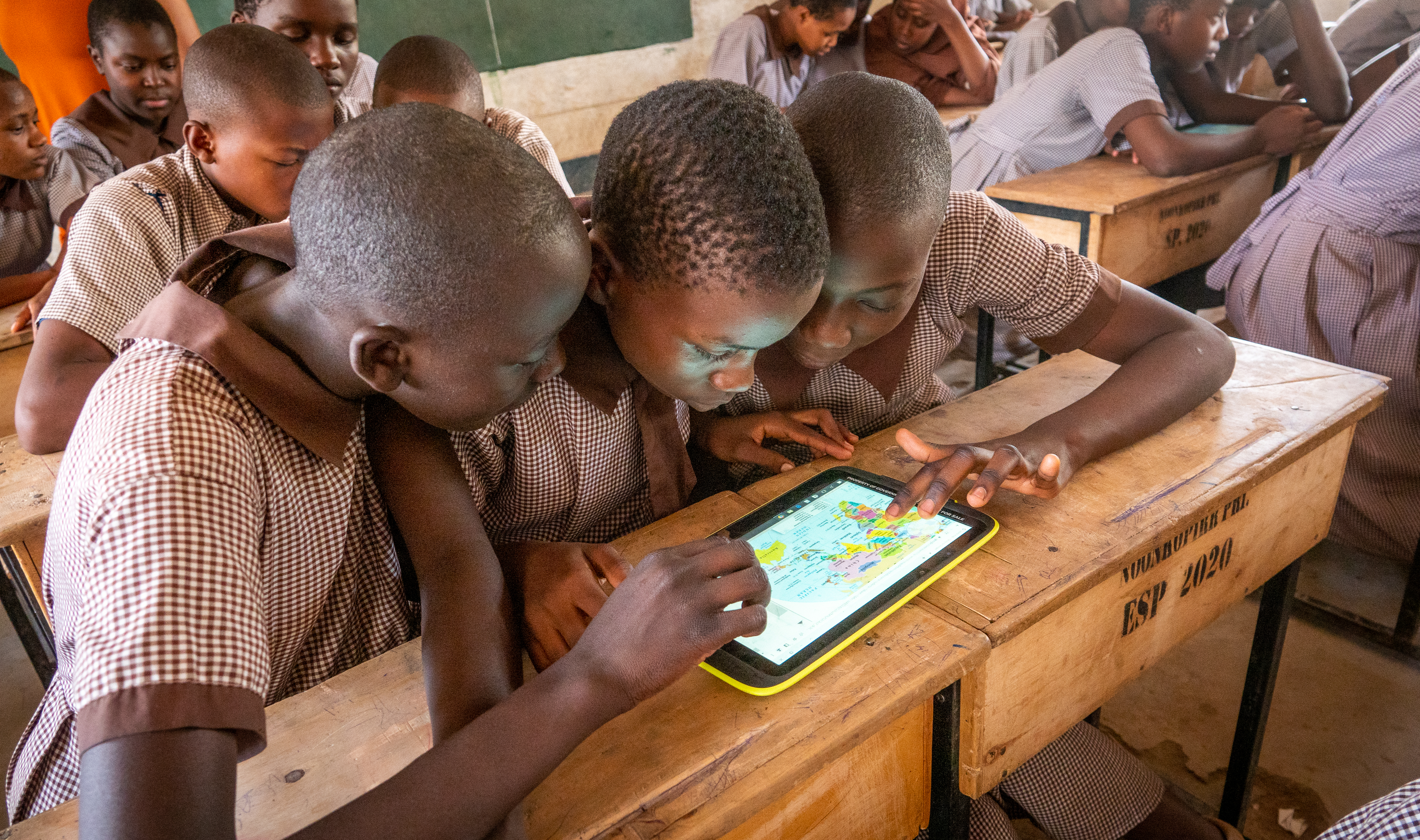 Trois jeunes filles du Kenya consultent une carte du monde sur un iPad dans une école.