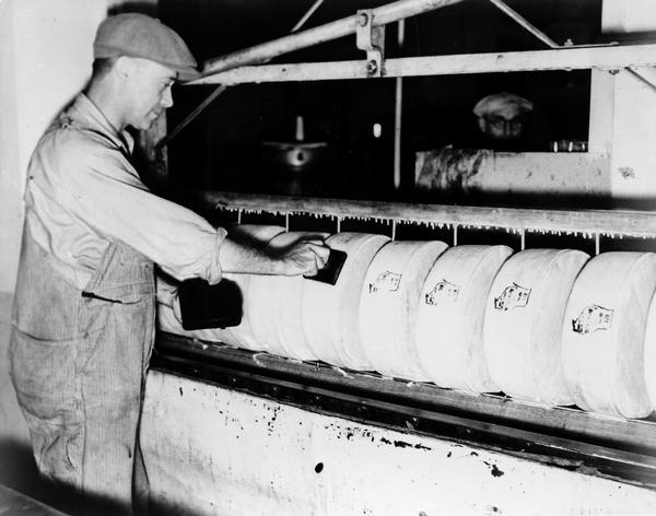 Un ouvrier d'une fromagerie de New Glarus appose un tampon du Wisconsin sur le fromage, 1922.