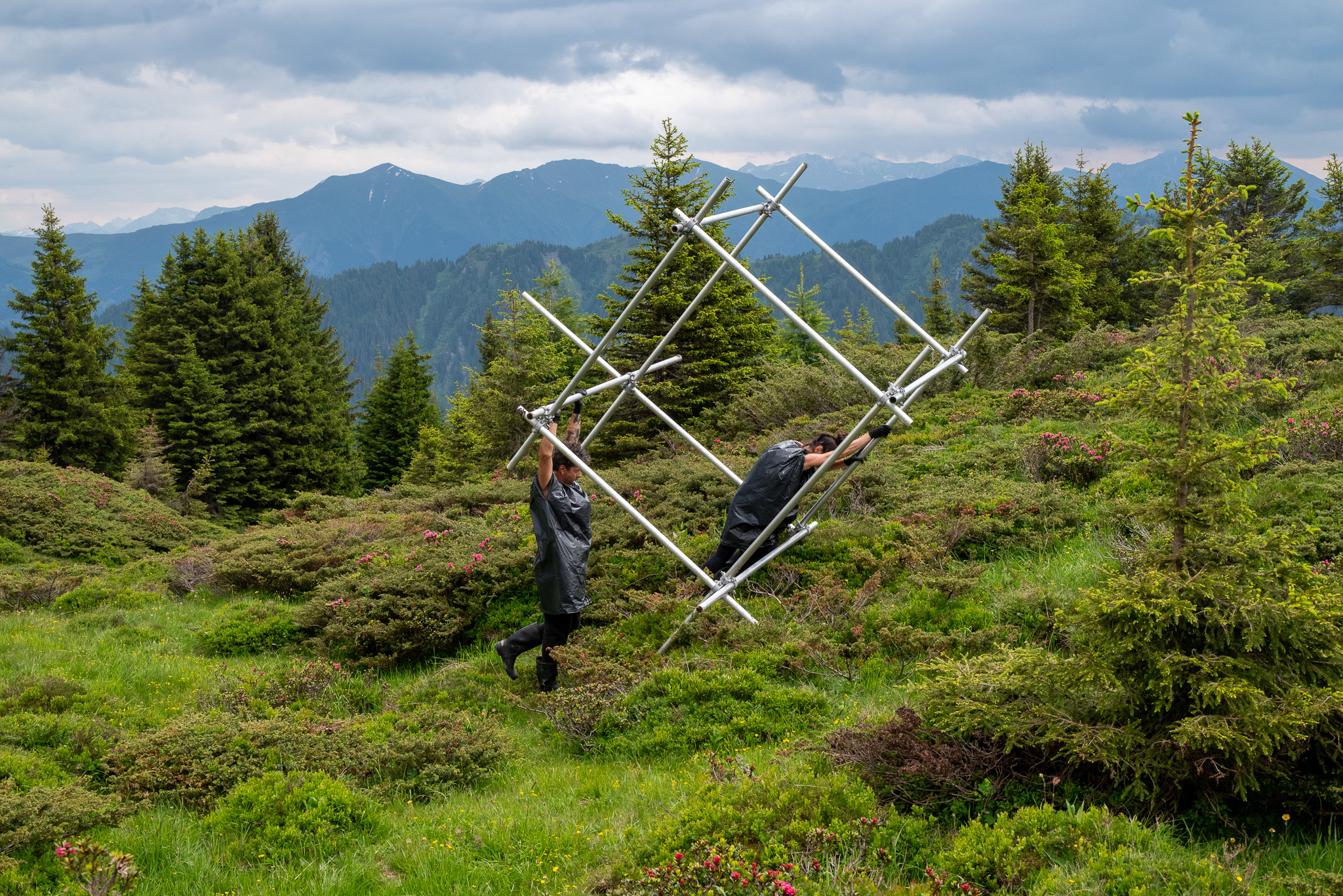 Deux personnes déplaçant un cube en tubes d'aluminium sur un alpage.