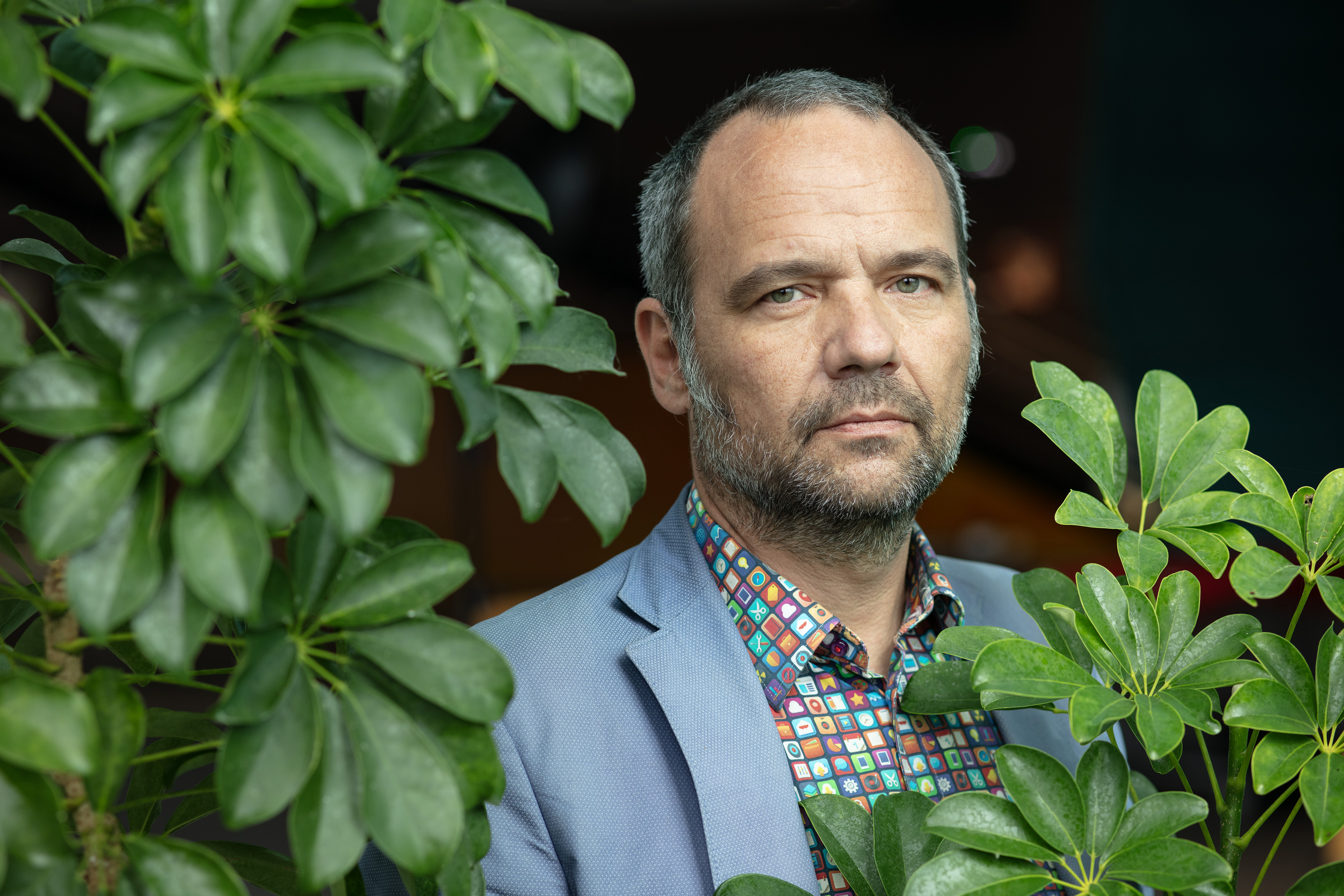 Homme barbu posant au milieu de plantes vertes.