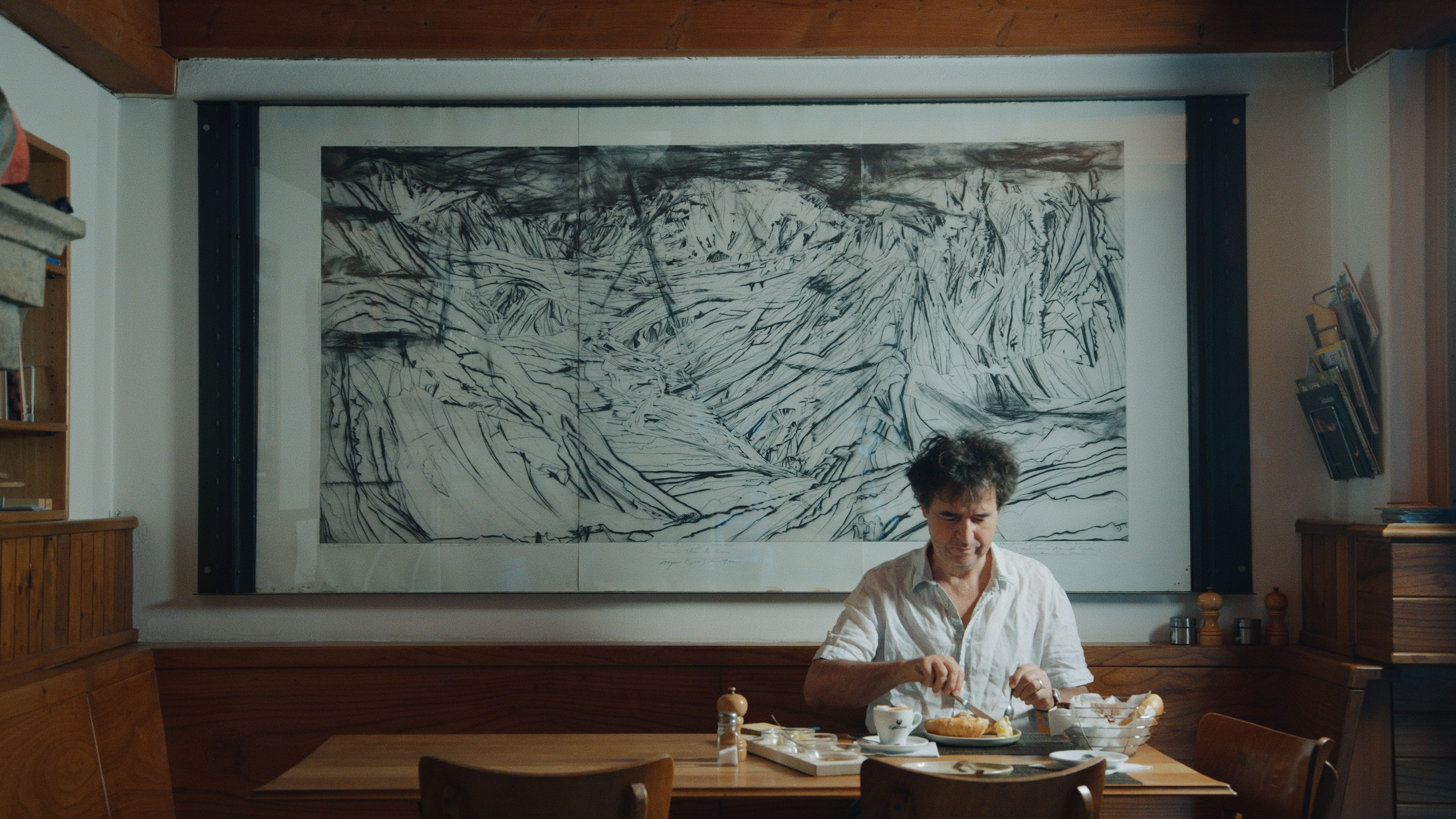 Homme assis en train de manger avec un grand tableau derrière lui