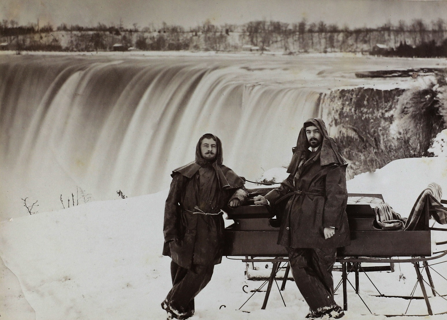 Deux hommes appuyés à un traineau à neige près d'une chute d'eau.