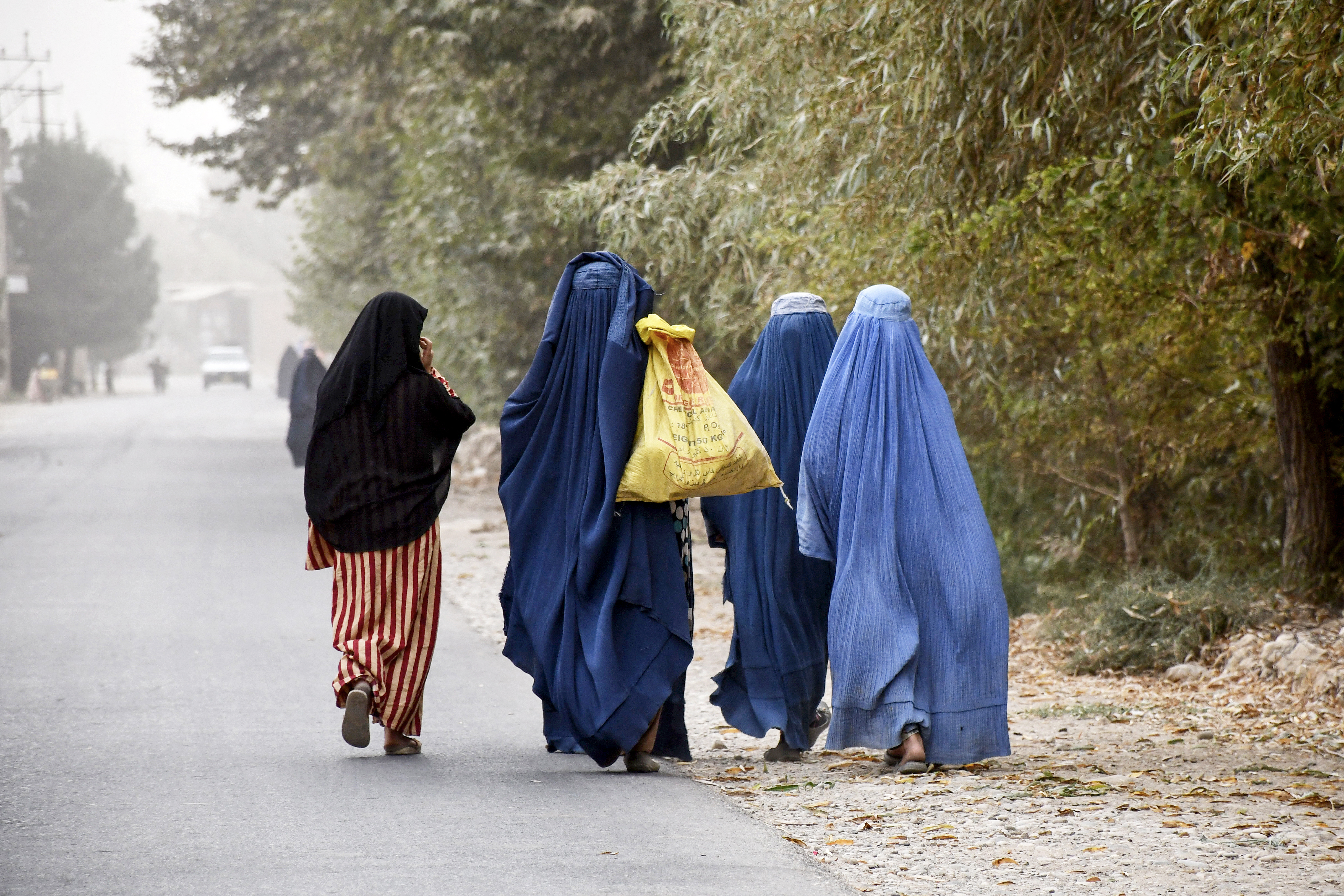 Quatre femmes afghanes en burqa marchant dans une rue.