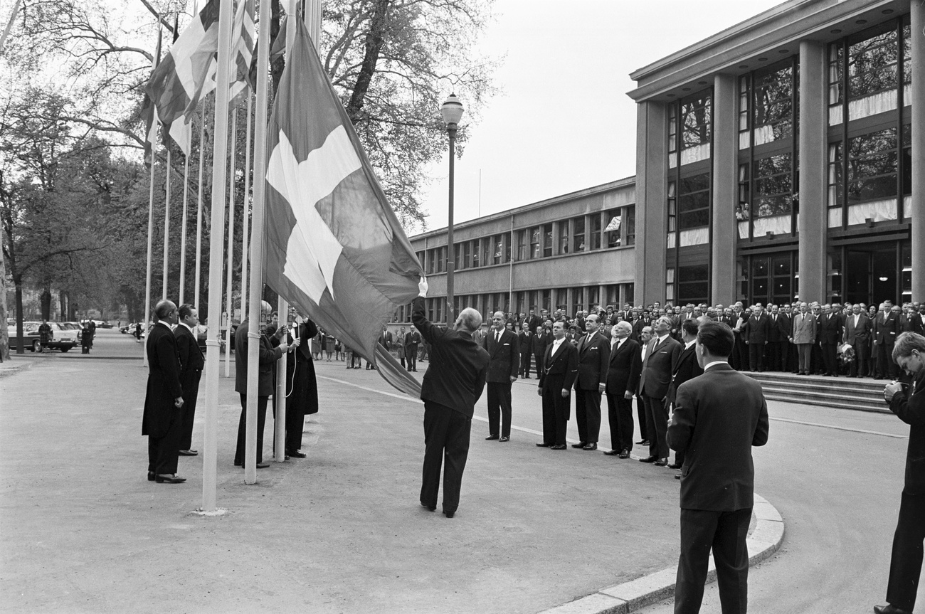 Foule hissant un drapeau suisse devant un bâtiment.