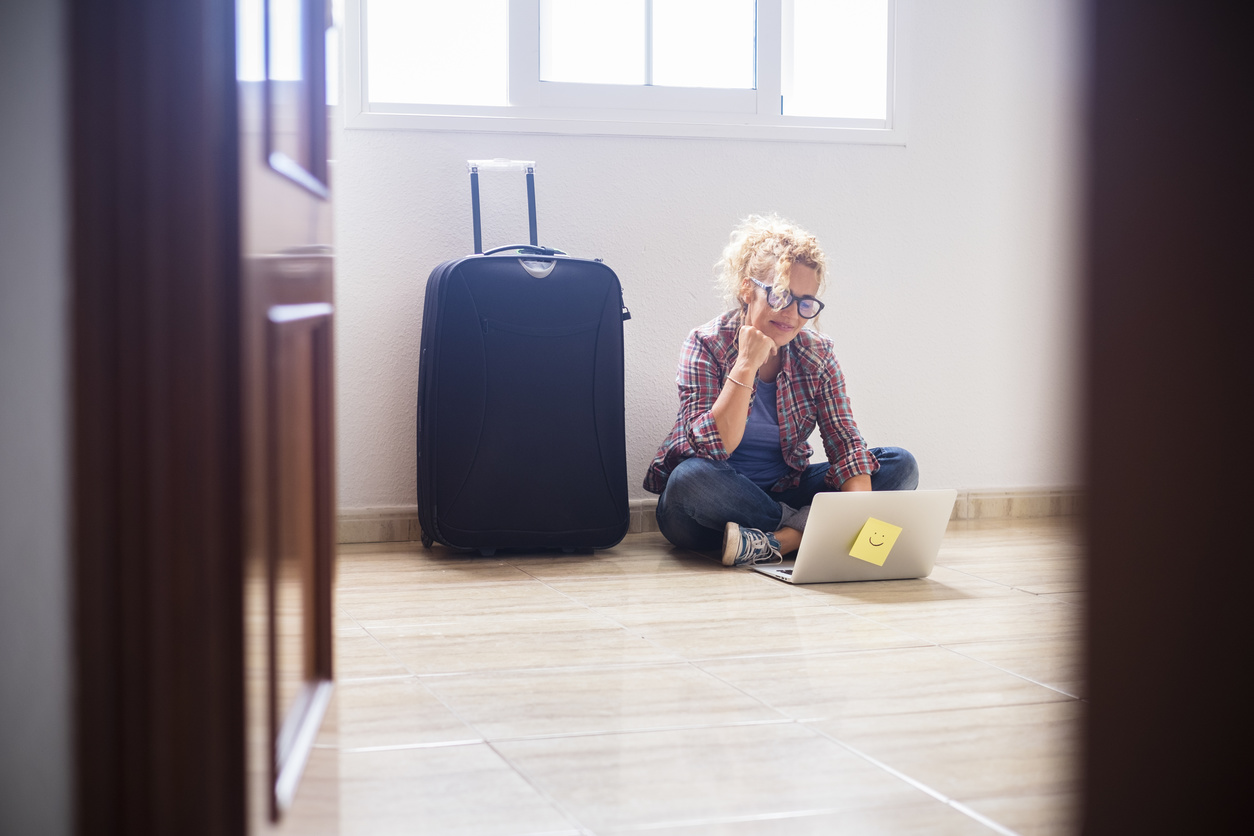 Jeune femme assise par terre dans une pièce vide avec un ordinateur portable et une valise