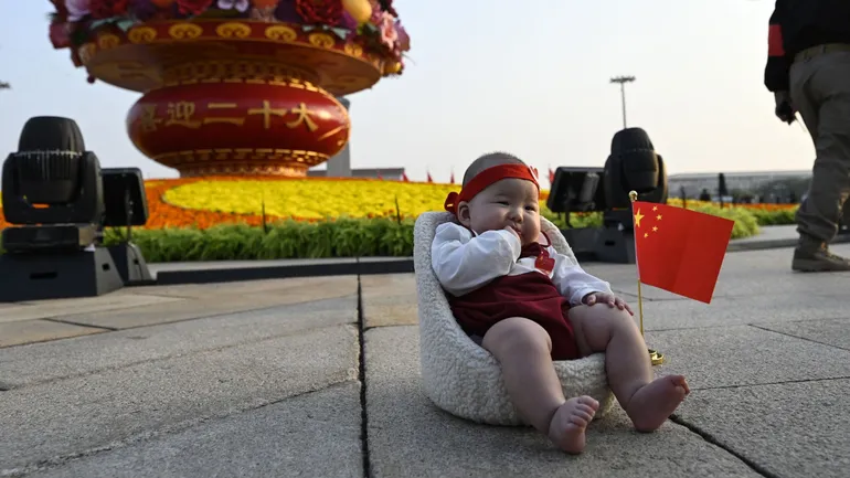 Une femme prend en photo un bébé devant une installation célébrant la prochaine fête nationale et les 20ᵉ Congrès du Parti communiste, sur la place Tiananmen à Pékin, le 29 septembre 2022.