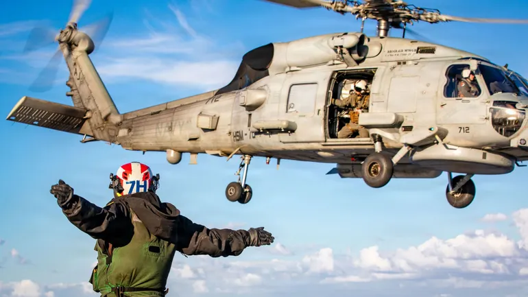 Sur ce document diffusé par l’US Navy, un marin américain signale le décollage d’un hélicoptère MH-60R Sea Hawk, appartenant à l’escadron d’attaque maritime 70 (HMAS 70), sur le pont d’envol du plus grand porte-avions du monde, l’USS Gerald R. Ford (CVN 7